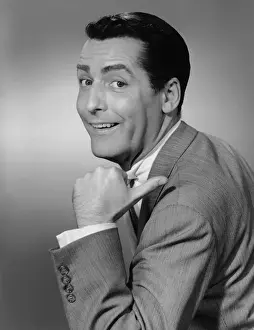 Smiling man pointing in studio, (B&W), portrait