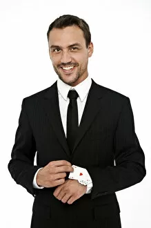 Smiling man wearing a suit pulling several aces out of his sleeve