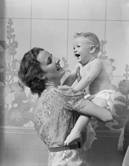 Smiling mother lifting her crying baby son, looking up at him Smiling mother lifting her crying baby son, looking up at him