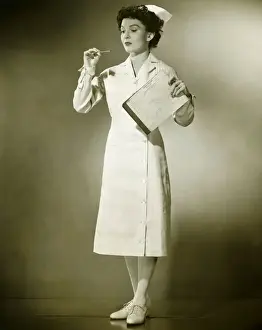 Thermometer Prints: Smiling nurse holding thermometer and files in studio, (B&W), portrait