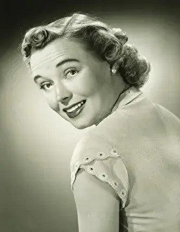 Smiling woman looking over shoulder in studio, (B&W), portrait
