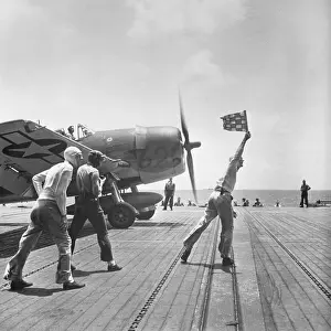Prints of A launching officer aboard the USS Bunker Hill gives the go signal to a Grumman Hellcat ready for take off Unveiling History: Soldier Signaling to Grumman Hellcat