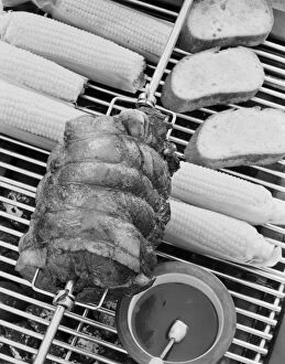 Images Dated 16th August 2011: Spit roasting of ham on barbecue grill with corn cobs, close-up