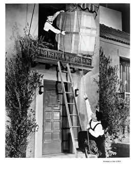 Prints of Stan Laurel on the 2nd story of a building lowering a large crate down to the ground where Oliver Hardy is ready to receive it in a scene from the film The Music Box, 1932 Timeless Comedy Icons: Classic Moments from the Legendary Duo: Stan Laurel And Oliver Hardy In The Music Box