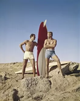 Sufers with surfboard standing on beach, smiling