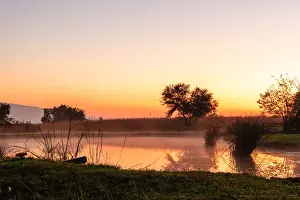 The sun rises over a small dam in the high veld winter landscape near Hartebeespoort, South Africa