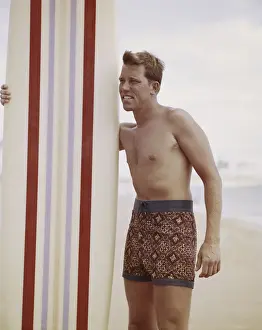 1963 Prints: Surfer holding surfboard on beach