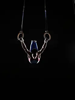 Balance Prints: Teenage (16-17) male gymnast practicing on rings against black background