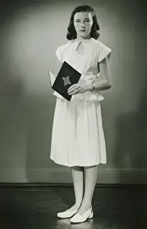 Sundress Prints: Teenage girl (13-14) in white dress standing in studio with open book, (B&W)