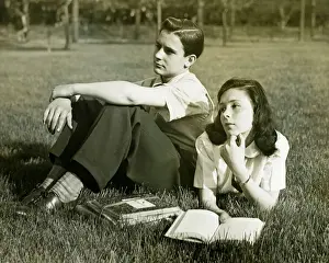 Girlfriend Prints: Two teenagers resting in field, boy (16-17) sitting, girl (14-15) lying with book, (B&W)