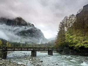 Rain Gallery: Torrent of high mountain with a bridge of wood in a valley with mountains and forests in autumn