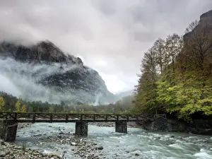 Overcast Prints: Torrent of high mountain with a bridge of wood in a valley with mountains and forests in autumn