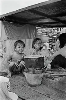 Prints of Two smiling Vietnamese children sitting beside a cooking pot in a makeshift shelter in Saigon, Vietnam, 30th August 1965 Vietnam Prints: Vietnamese Children, Saigon