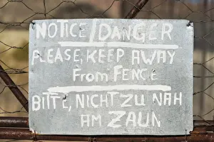 Dangerous Prints: Warning sign in English and German on the fence of a predator enclosure, Namibia
