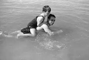 Prints of 8th October 1938: English jockey Gordon Richards (1904 - 1986) swimming near his home in Shoreham, West Sussex, with his son Jackie Chronicling Britain's Story in Pictures: Water Jockey