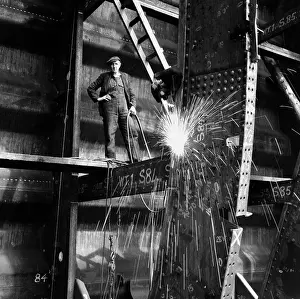 Welder on beam in shipyard, portrait (B&W)
