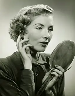 Blonde Hair Prints: Woman adjusting earring, holding hand mirror, (B&W), portrait