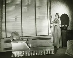 Blinds Prints: Woman adjusting window blind in living room, (B&W)
