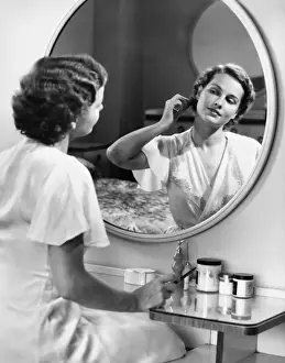 One Mid Adult Woman Only Prints: Woman doing hair in front of mirror, (B&W)