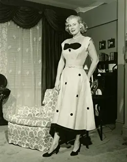 Black Colour Prints: Woman in fashionable dress standing by armchair in living room, (B&W), portrait
