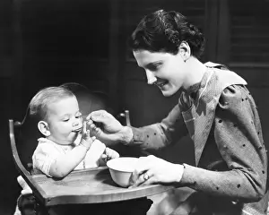 6 11 Months Prints: Woman feeding baby (6-9 months) sitting on high chair (B&W)