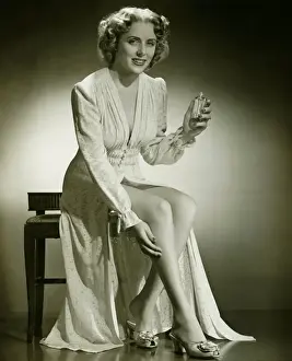 Woman in gown sitting on stool, holding perfume, (B&W), portrait