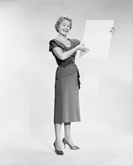 1960s Fashion Gallery: Woman holding blank piece of paper, portrait, studio shot