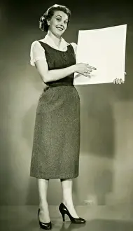 25 30 Years Prints: Woman holding blank sheet of paper, posing in studio, (B&W), portrait