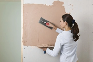 Woman holding a plastering hawk and spreading plaster on to a wall with a trowel Woman holding a plastering hawk and spreading plaster on to a wall with a trowel