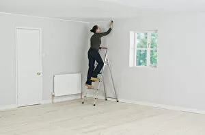 Woman on ladder painting edge of ceiling