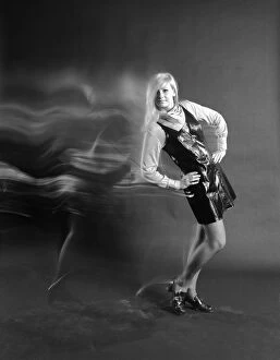 Blurred Motion Gallery: Woman with long blond hair wearing vinyl dress and scarf around neck with hands on hips