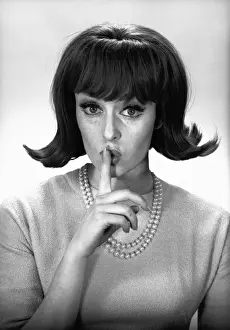 Woman making silence gesture in studio, (B&W), portrait