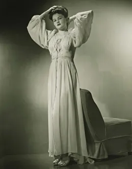 35 39 Years Collection: Woman in nightdress standing by chair in studio, (B&W)