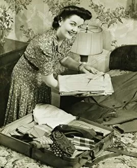 Woman putting clothes into suitcase, (B&W)