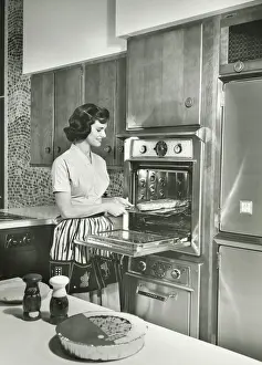 One Mid Adult Woman Only Prints: Woman putting meal into oven in kitchen, (B&W)