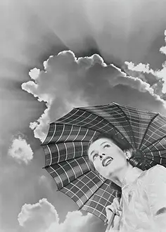 One Mid Adult Woman Only Prints: Woman in raincoat holding umbrella looking up into sky of dark clouds and impending storm