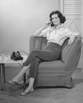 Woman sitting on armchair, talking on phone, (B&W)