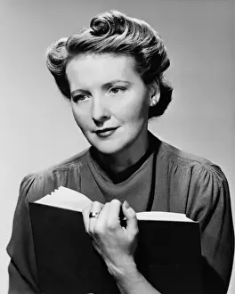Woman sitting holding book, (B&W), portrait