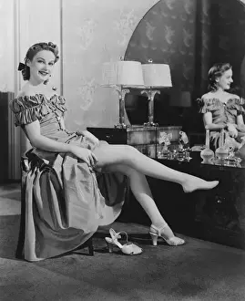 Woman sitting at vanity table, putting on stockings, (B&W), portrait