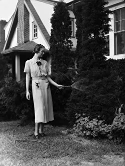 Woman spraying flower bed with garden hose