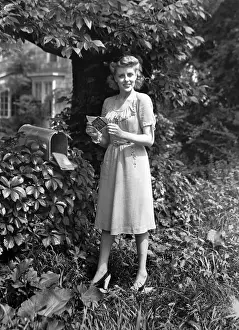Woman standing at mailbox, holding letter, (B&W), portrait