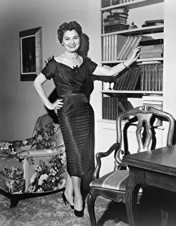 Bookshelf Prints: Woman standing in rich living room with hand on shelf, (B&W)