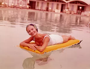 Swimming Gallery: Woman in swimming pool reclining on inflatable raft, wearing bathing cap, smiling