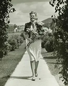 Woman walking on path, holding bunch of field flowers, (B&W)