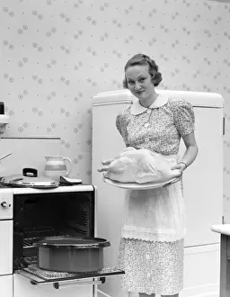 Three Quarter Length Prints: Woman Wearing An Apron Over A White Collar Cotton Print Dress Is Standing In Front Of An