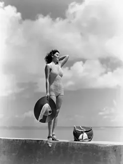 Suit Prints: Woman Wearing Knit Bathing Suit Standing Wall Ocean Sea Background Holding Sun Hat Beach Bag Sail Boat Fashion Beauty