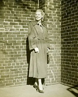 Raincoat Prints: Woman wearing mackintosh standing at brick wall outdoors, (B&W)