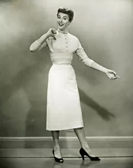 1960s Fashion Collection: Woman in white dress pointing to herself in studio, (B&W), portrait