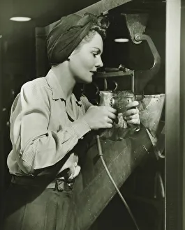 Bib Overalls Gallery: Woman working with electric drill in factory, (B&W)