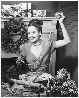 Woman wrapping Christmas presents in living room, (B&W), portrait